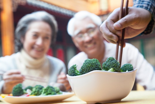close up of a bowl of broccoli with grandparents looking at it in the background