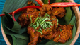 Traditional rendang ayam served on a wooden bowl with banana leaves and garnished with whole chilli.