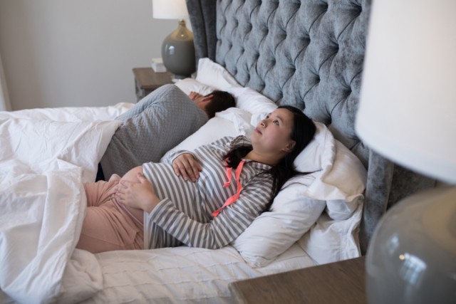 pregnant woman looks up with her husband in bed next to her