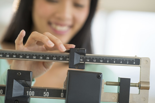 Woman measuring her height and weight to check her body mass index (BMI)