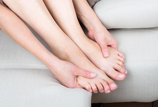 A lady sitting on the couch, massaging her feet