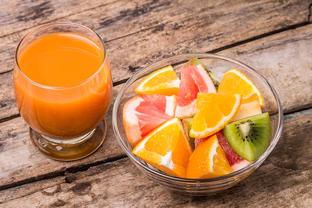 A cup of fruit punch and a bowl of freshly cut fruits on a wooden table