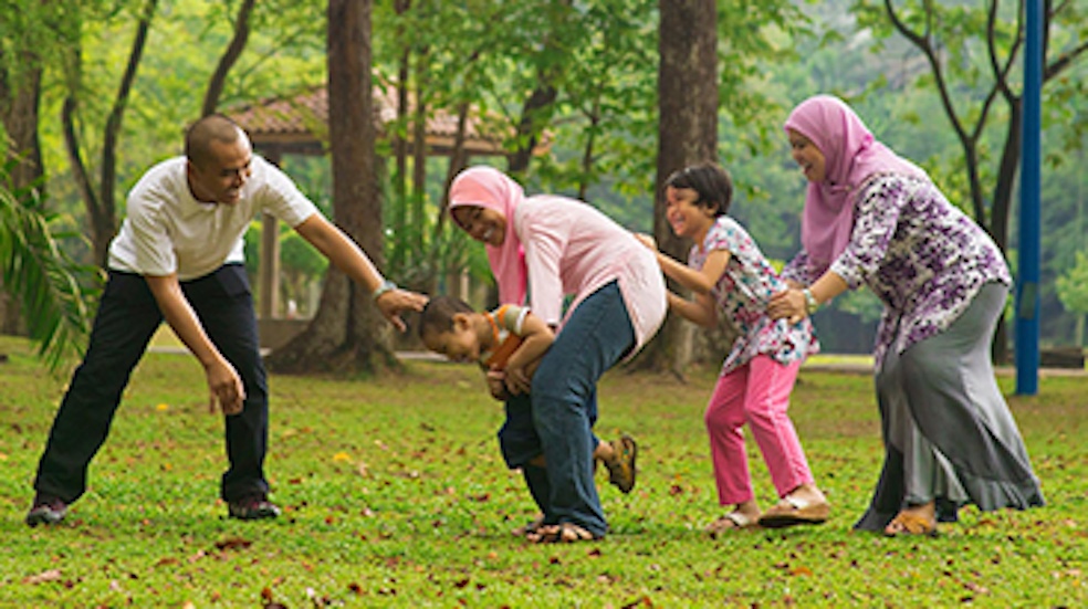 Family playing together outdoors on grass, laughing and chasing each other.