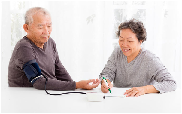 elderly asian woman taking and recording blood pressure for her husband