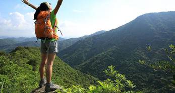 Young woman hiking overseas, with a water bottle, hand sanitizer, healthy snacks, and cold and flu medication in her backpack.