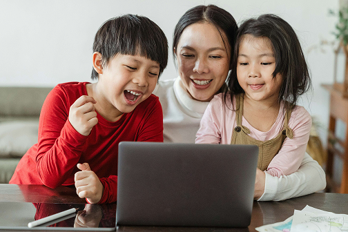 Mother and two children smiling and using a laptop together.