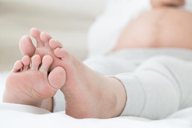 Pregnant mom sitting in bed and resting her legs to prevent swelling