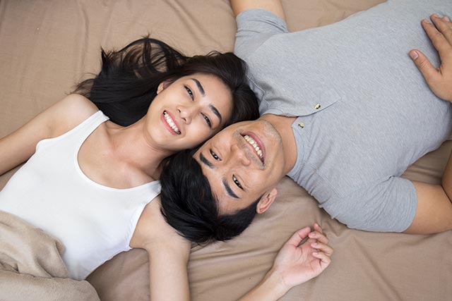 A young couple lying in bed and smiling at the camera