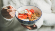 A young woman holding a bowl of granola and strawberies with yoghurt for breakfast