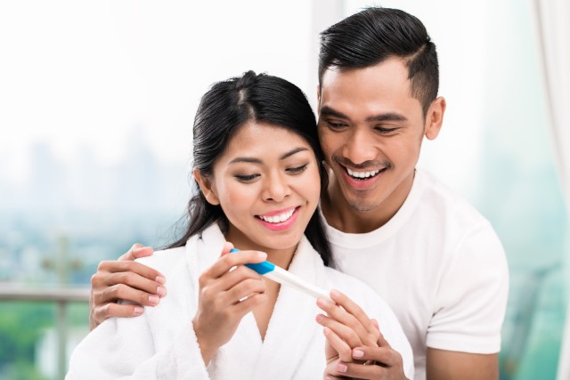 pregnant woman looking at a pregnancy kit and smiling with husband