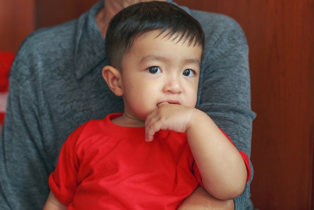 asian boy in red sucking his thumb while being held