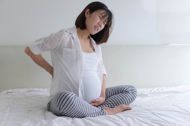 pregnant asian woman clutching her back
