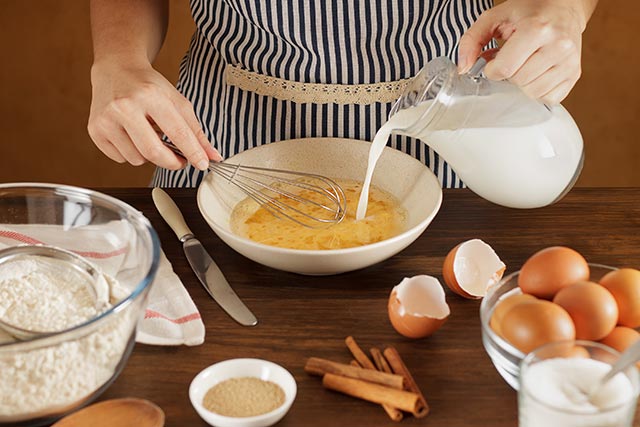 A lady adding milk into her egg yolk mixture