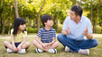 A father sitting on the grass and talking with his son and daughter