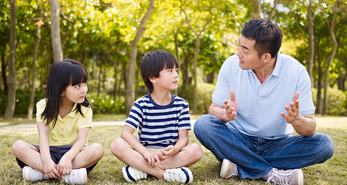 A father sitting on the grass and talking with his son and daughter