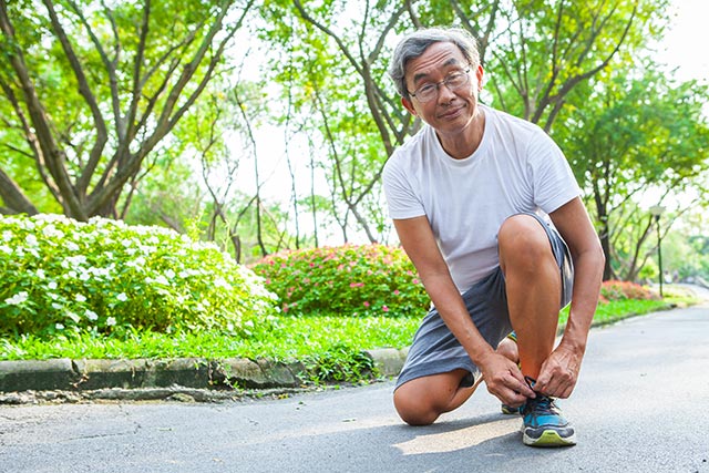 Senior man tying his shoelaces and getting ready for a run in a park