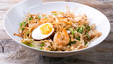 A bowl of fried noodles, with prawns, vegetables, furikake and half boiled egg