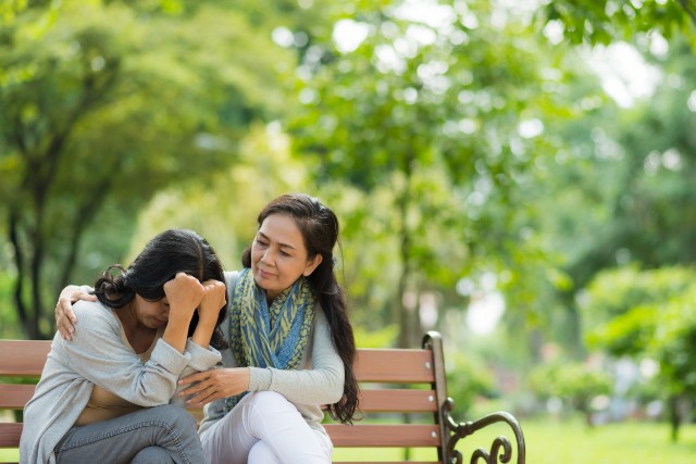 a woman consoling another on a park bench
