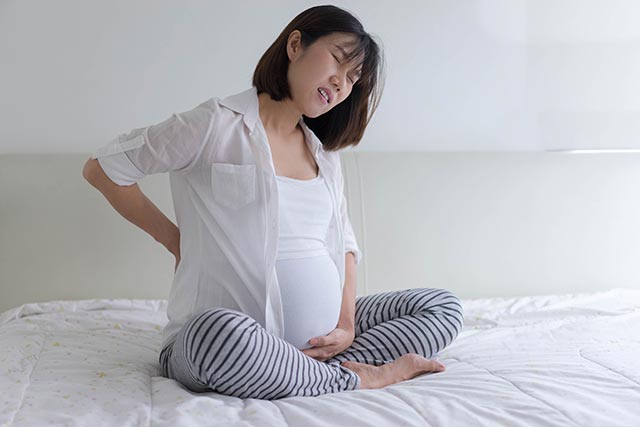 Pregnant mother sitting on the bed with a backache