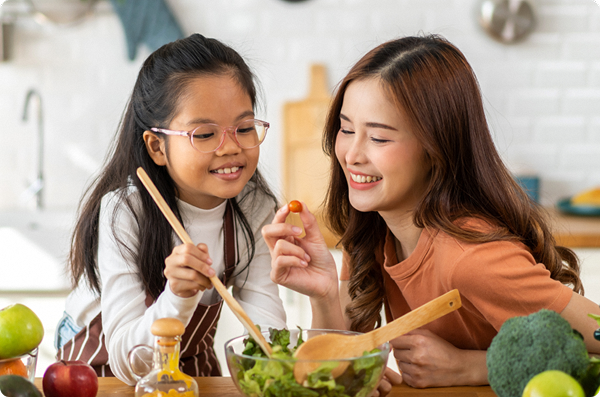 Mother and child preparing a salad together, smiling while mixing vegetables in the kitchen.