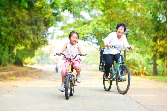 asian elderly woman riding a bicycle next to a young child