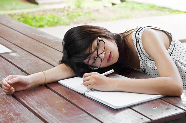 a tired asian woman falls asleep on a bench while writing on her notepad