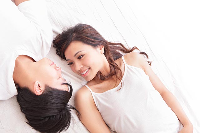 Young woman lying in bed and looking at her boyfriend besides her lovingly