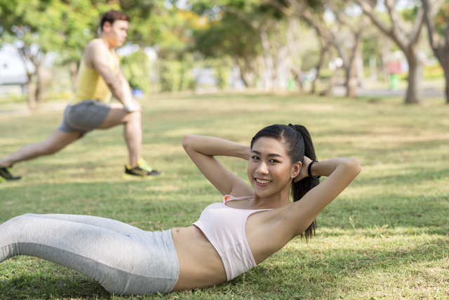 Young woman leading an active lifestyle as advised by Health Promotion Board by doing sit-ups at the park.>