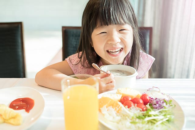 A young girl sitting at the table smiling while having breakfast