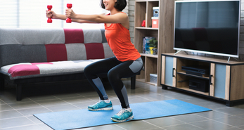 A woman doing squats with small dumbbell indoors.