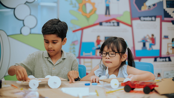 Children creating a model car with craft materials in a classroom.