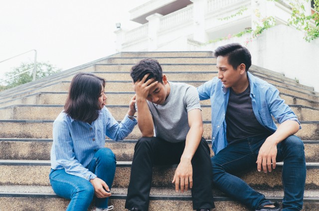 two malay teenagers console their friend while sitting on a staircase outdoors