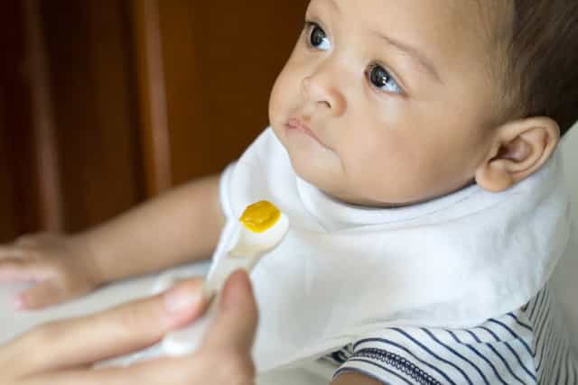 feeding a baby solid food puree on a baby spoon, waiting to see any signs baby is ready for solid food.>