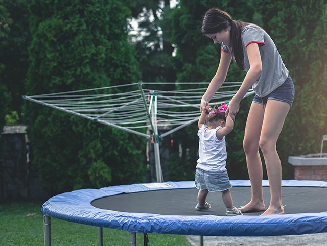 Young girl playing on the trampoline with her little sibling