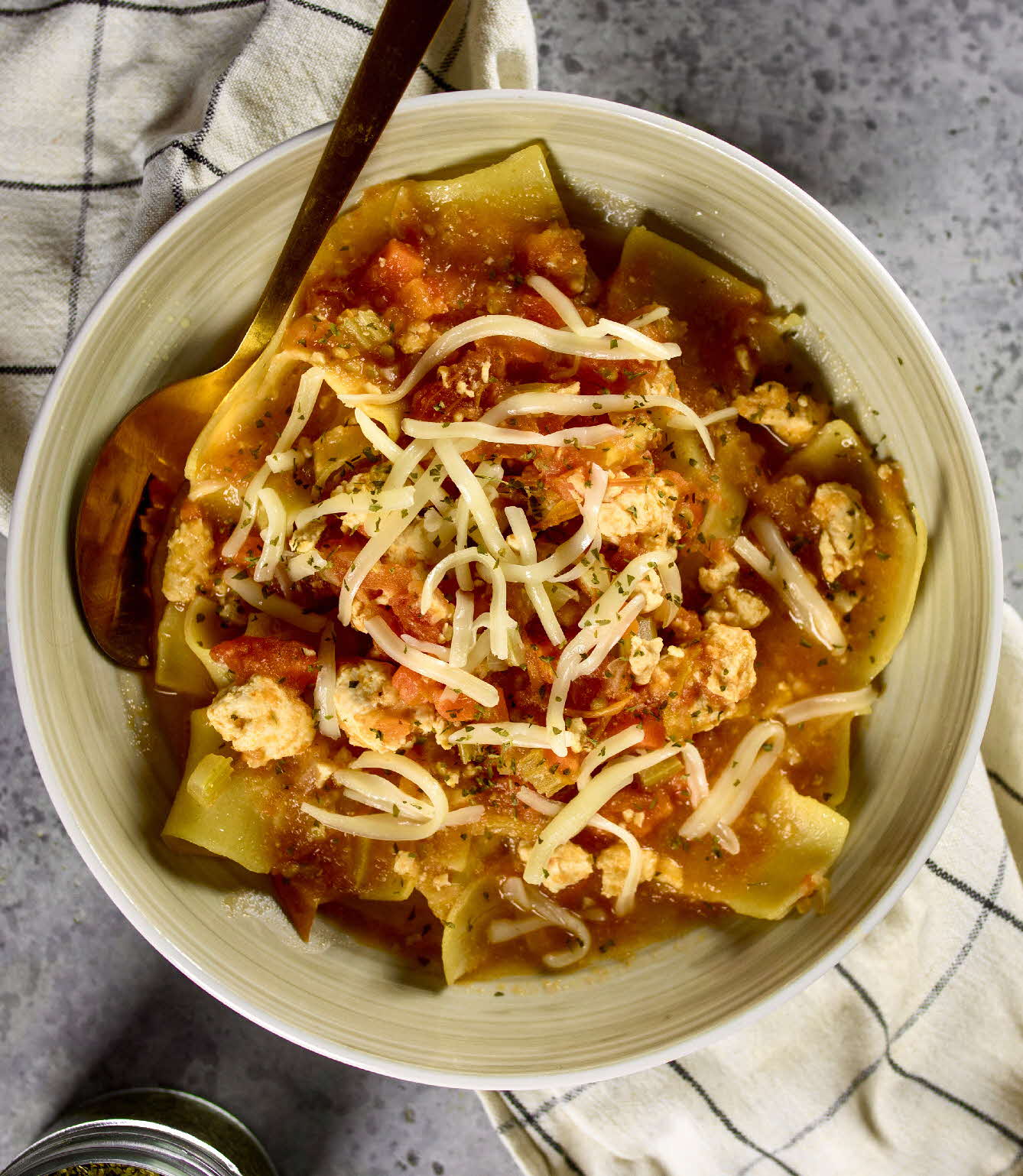 A bowl of one pot lasagna soup topped with shredded cheese and parsley.