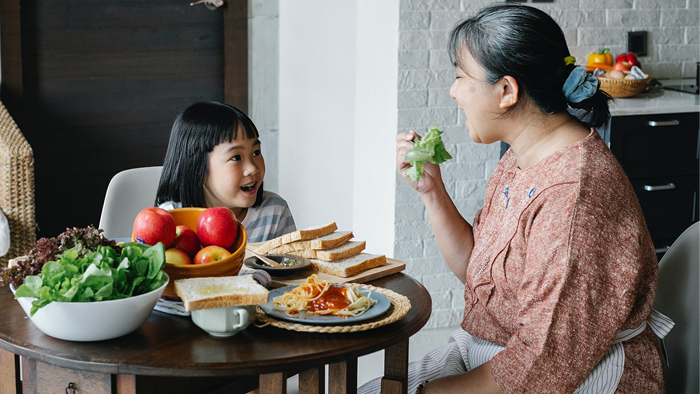 Mother and child having a meal together, with the mother eating vegetables at the table.