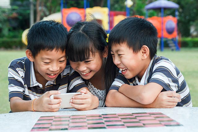 Young kids huddling around and playing on the phone