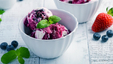 A bowl of blueberry ice cream on a white counter with fresh berries