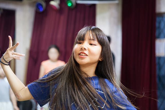 young asian girl dancing in a studio while her friends watch in the background