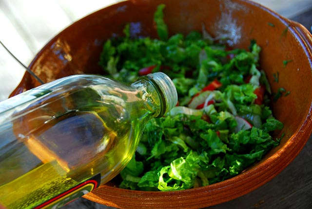 pouring olive oil into a salad as a dressing
