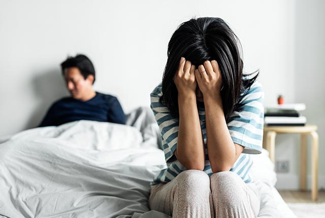 A couple sitting separately on the bed after an argument