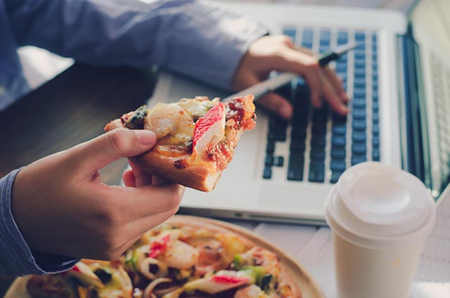 Business man eating pizza at his desk while working on a project