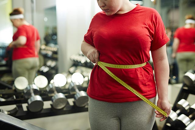 Overweight woman measuring her waist circumference in the ym