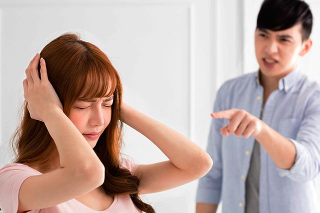 A young girl covering her ears with her hands while a guy scolds her