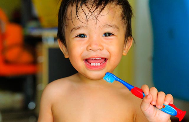 a happy young boy is smilling while brushing his teeth