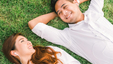 a couple laying on the grass, and facing each other, with big smiles on their face