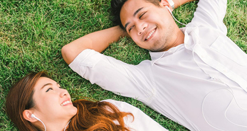 a couple laying on the grass, and facing each other, with big smiles on their face