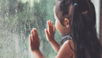 Young girl staring out a window and looking at the rain