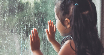 Young girl staring out a window and looking at the rain