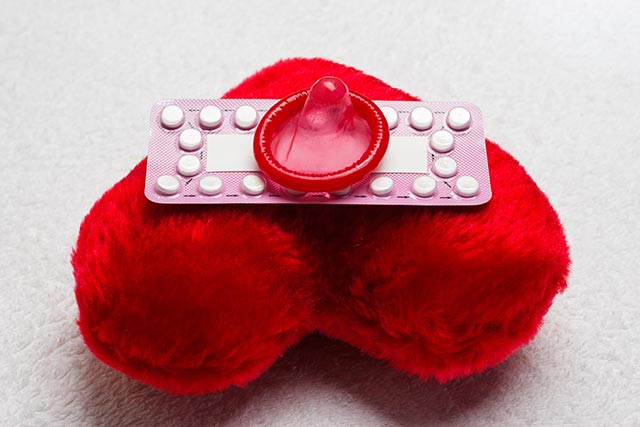 Contraceptives on top of a fluffy red heart-shaped pillow